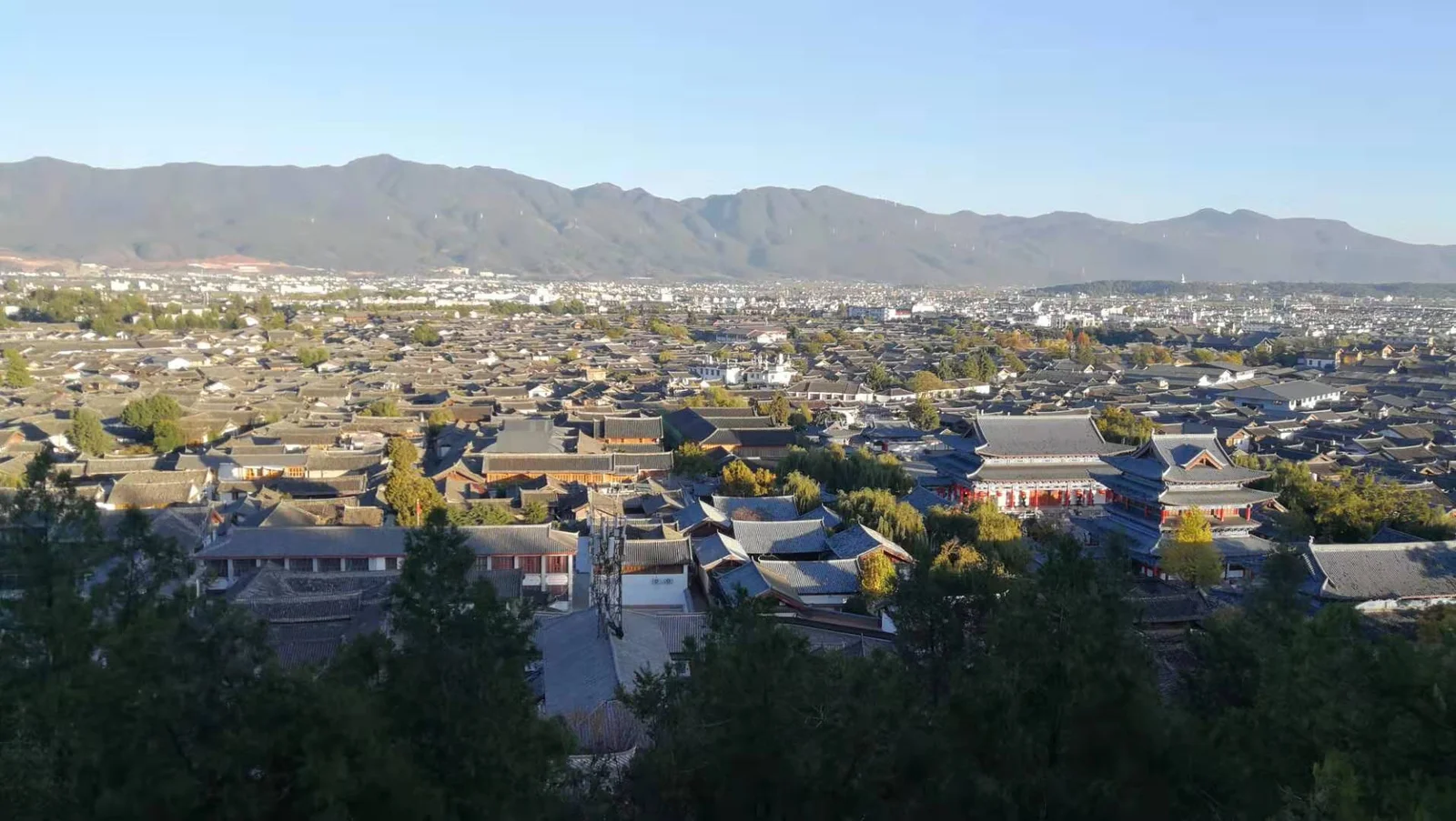 Traditional tiled rooftops of Lijiang Old Town below distant mountain ridges