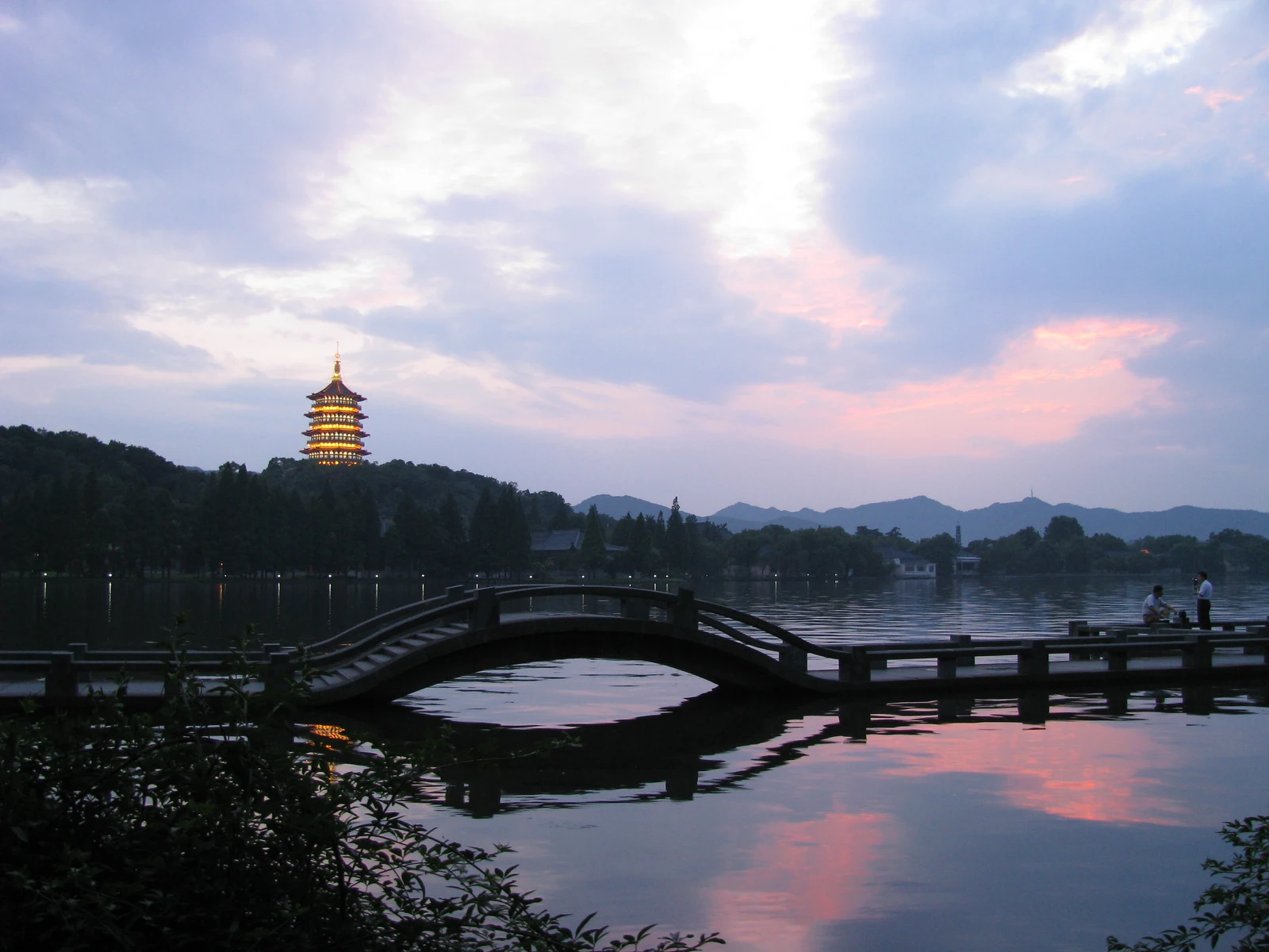 A curved bridge, Leifeng Pagoda and pastel sunset reflected in Hangzhou West Lake